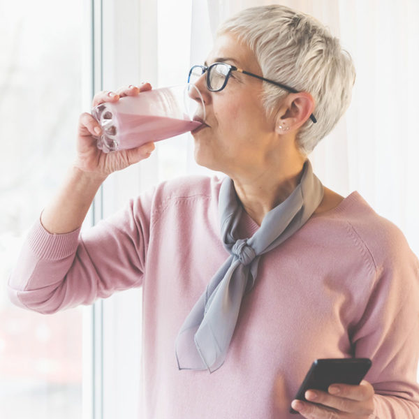 Senior woman drinking immune supporting meal replacement beverage while on her phone