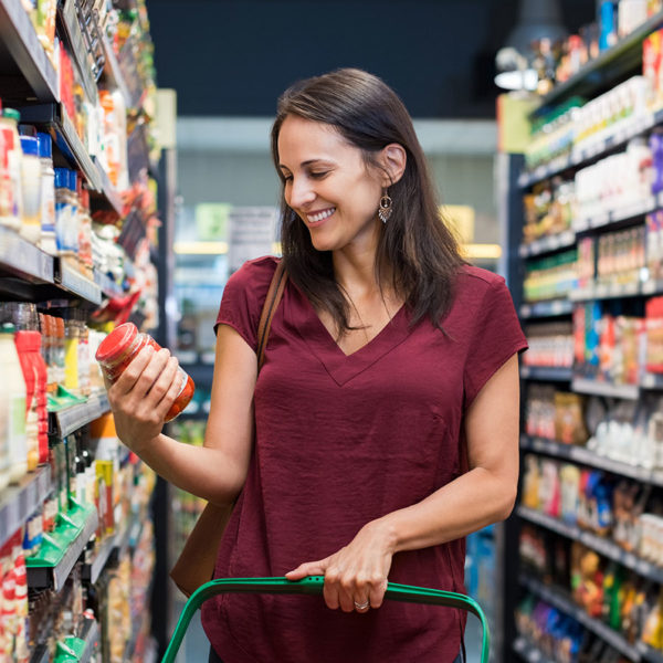 Woman grocery shopping looking at nutrition label on jar