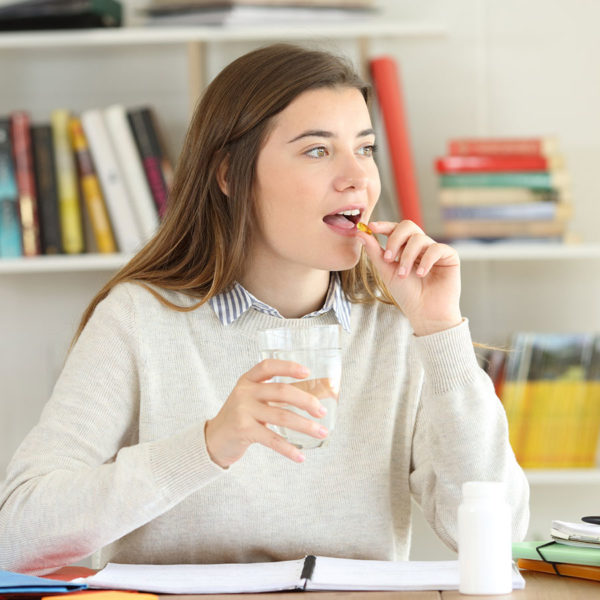 Woman taking supplement with glass of water at her desk