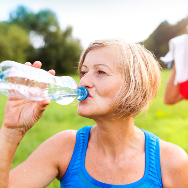 older woman drinking water outside after exercise